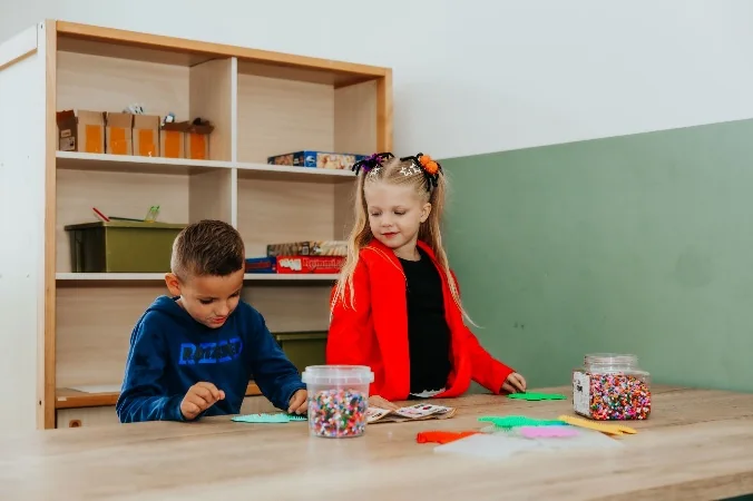 Twee kinderen zijn samen creatief bezig aan een tafel met knutselmaterialen.