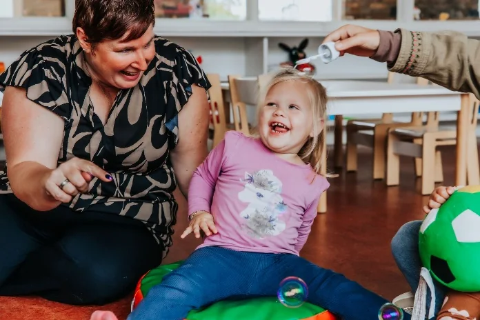 Een pedagogisch professional en een kind lachen samen tijdens het spelen
